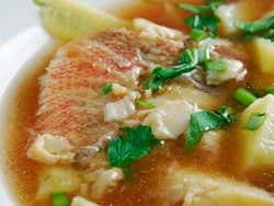 A close-up of a bowl of fish soup with garnish on top of it
