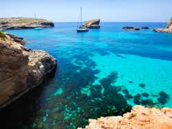 A view of a rocky cove with a boat sailing on the turquoise waters