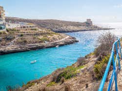 A small white boat in the middle of Xlendi Cove on a sunny day