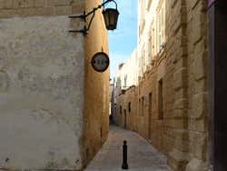 A narrow street with old stone and a speed sign on one of the walls