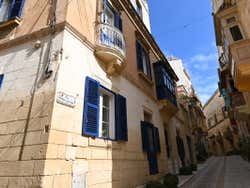 A narrow street in a city with royal blue shutters under a blue sky