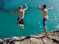 2 boys jumping into the sea from a rock