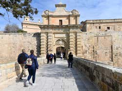 People walking through a large archeway to enter a city