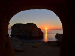 An orange sunset over the horizon seen through a sea cave