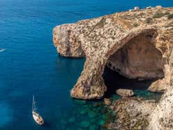 A sea cave with a white yacht sailing nearby it