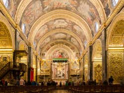 The interior of a cathedral with tall round ceilings with golden paintings on them