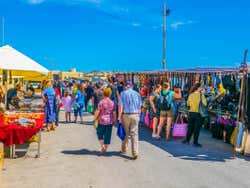 People walking around a market selling colourful produce on a sunny day