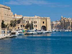 A coast with stone buildings and boats moored at a dock under a blue sky