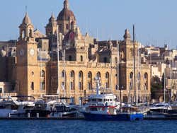 A city with towers and temples next to the sea with boats docked up at a pier
