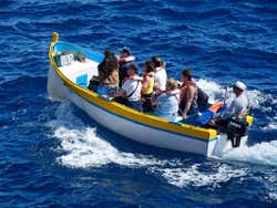 8 people sitting on a white, yellow and blue boat sailing through blue sea water