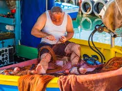 A man in a white vest cutting up a piece of red fishing net