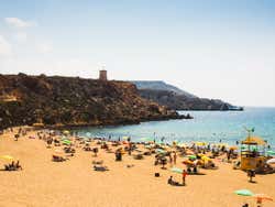 A sandy beach with several people lying on the beach under sun umbrellas