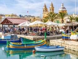 A dock with colourful boats at it and a temple seen inland