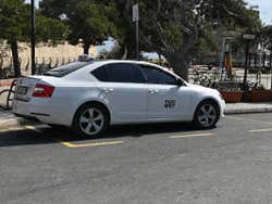 A white taxi parked on the side of the road at a taxi rank